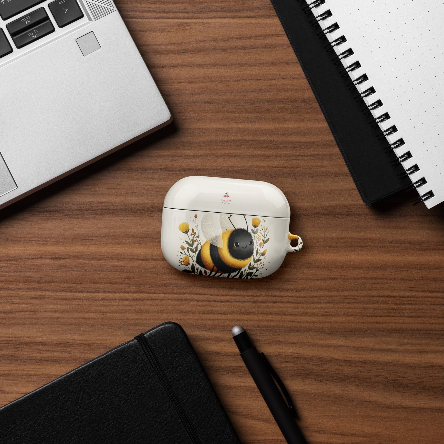 White case with a bee design on a wooden desk with a laptop, notebook, and pen.
