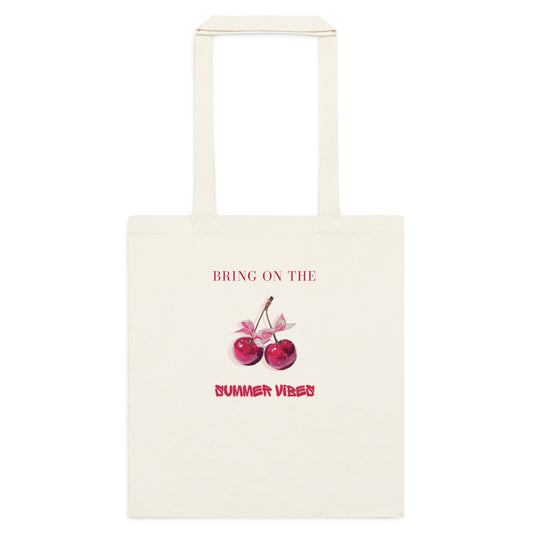 An off-white canvas tote bag with two top handles, featuring a graphic print of two red cherries with pink bows and the text 'BRING ON THE SUMMER VIBES' in pink, shown against a plain white background.