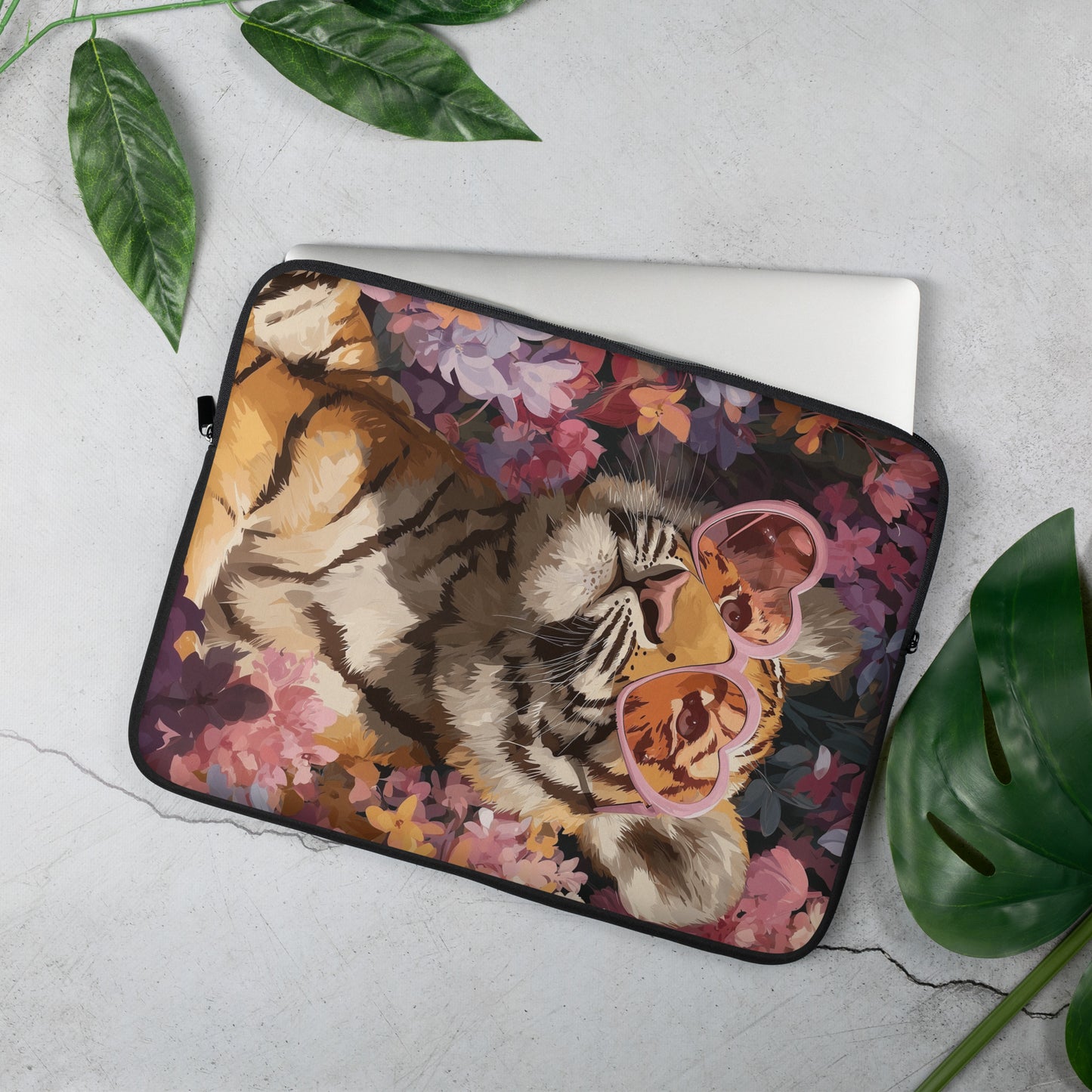 Artistic laptop sleeve featuring a bold tiger illustration wearing pink heart-shaped glasses, surrounded by purple and orange flowers, displayed as a product mockup on a light gray surface with green leaves.