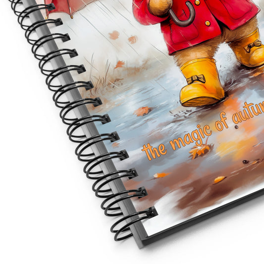 Spiral notebook with a cover featuring a bear in a red coat and yellow boots walking on a leaf-covered path with 'the magic of autumn' text.