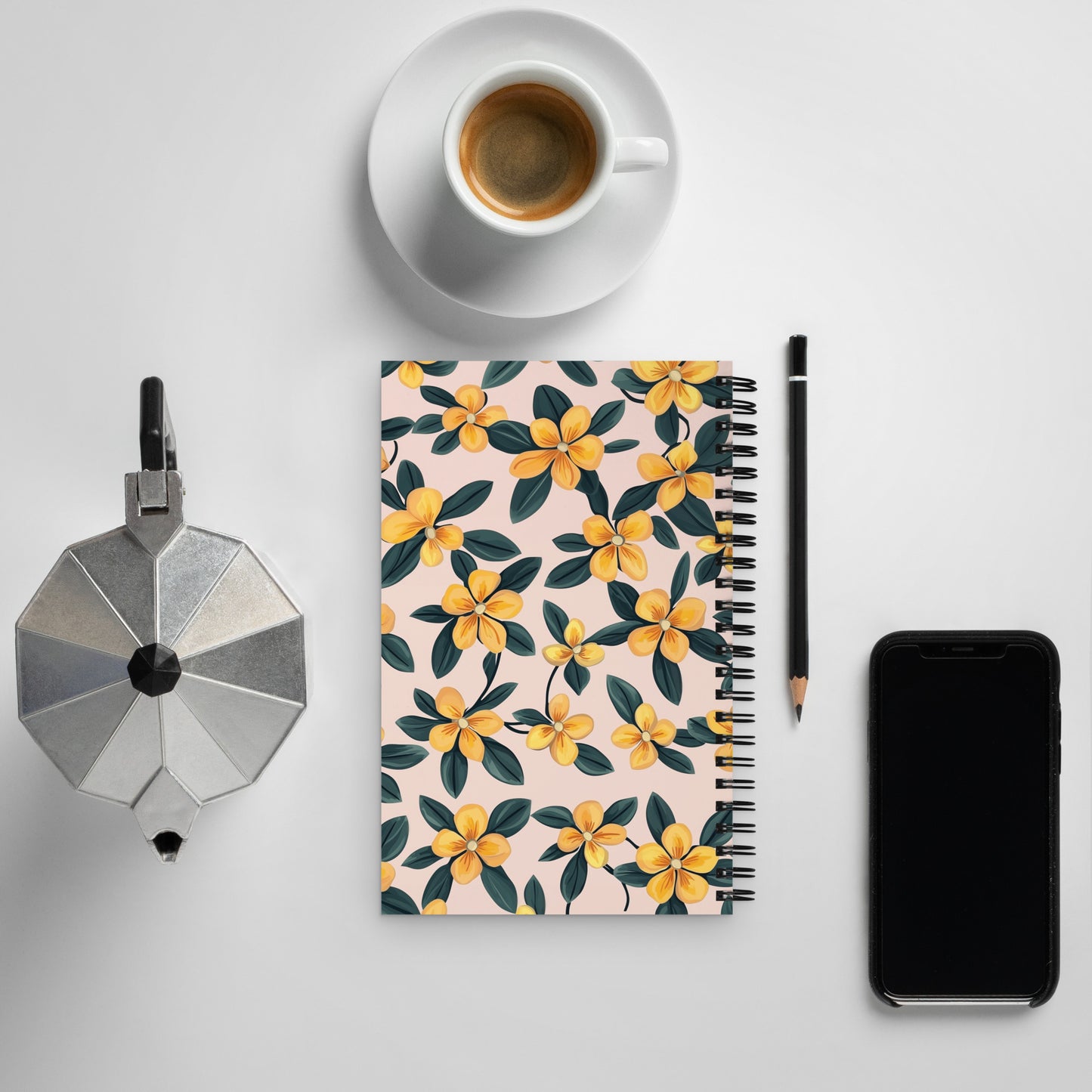 Spiral notebook with a delicate yellow and black floral pattern on a desk next to a coffee cup and a smartphone.
