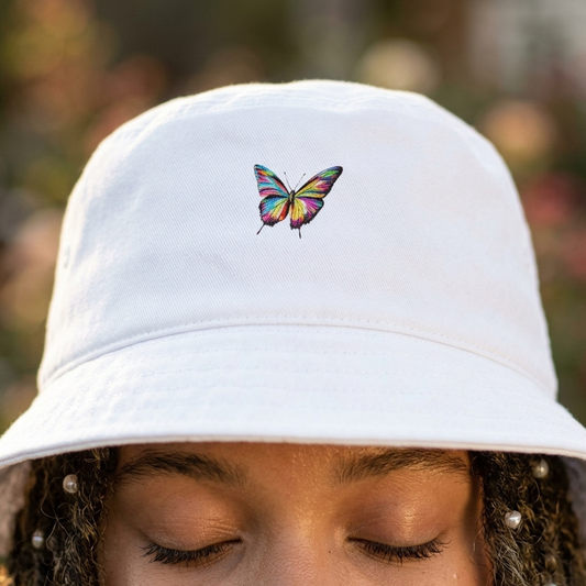 A woman wearing a white bucket hat with a colorful butterfly design, blurred natural background