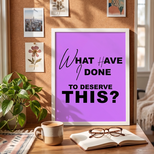 Framed poster with quote 'What have I dont to deserve this?' on a table with a cup, book, and glasses.