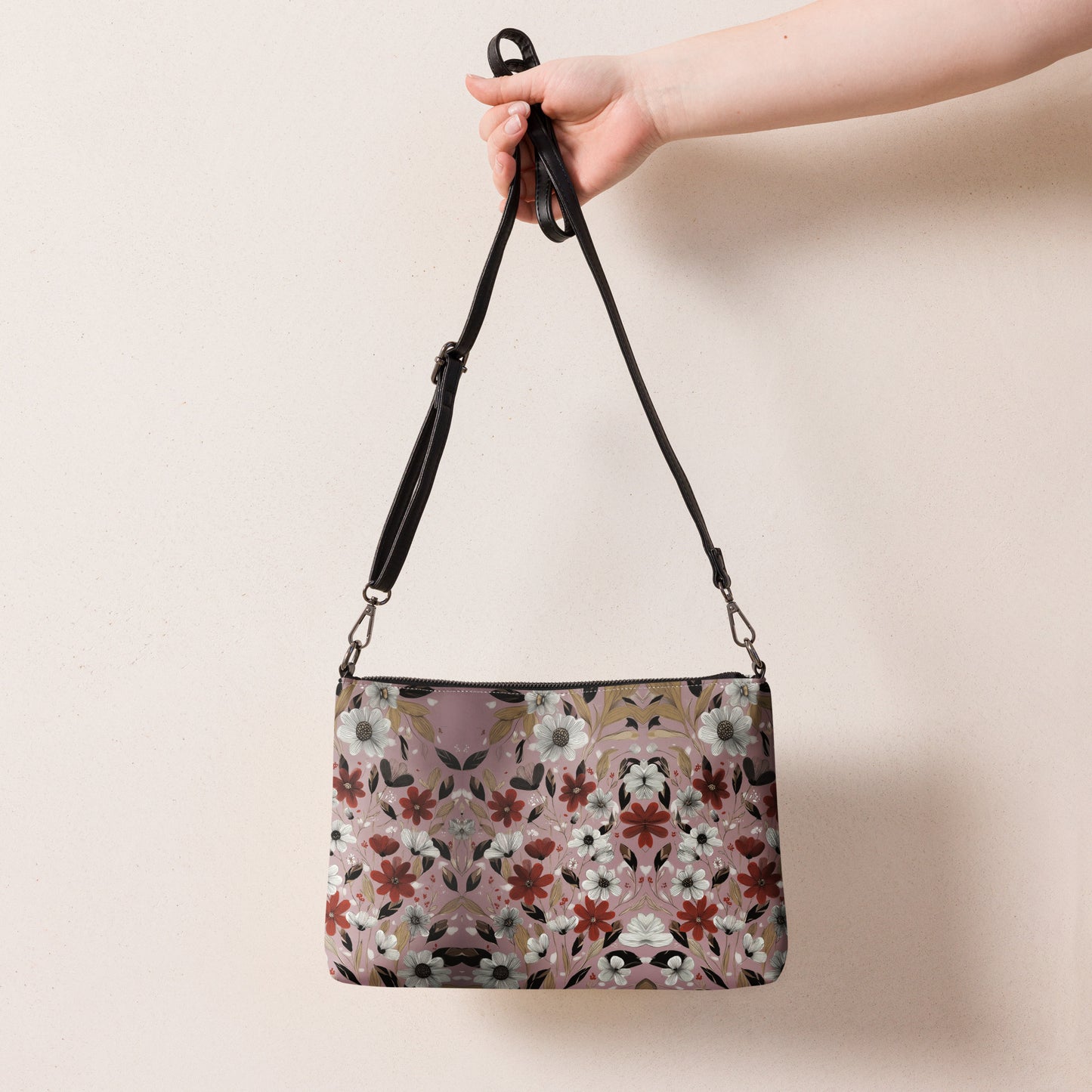 Floral patterned crossbody bag held by a hand against a plain background.
