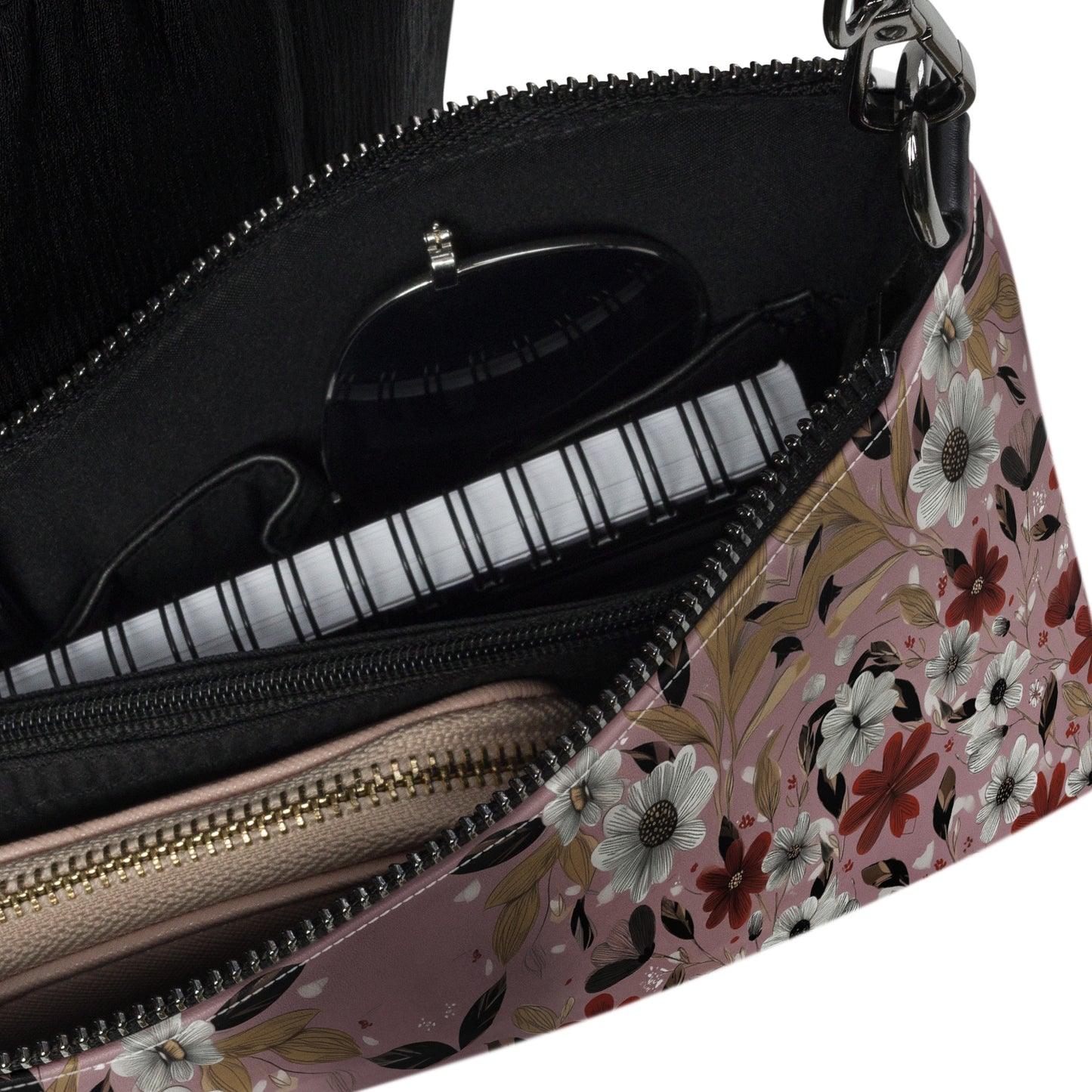 Close up of a floral patterned crossbody bag with its compartment revealing contents of the bag such as sunglasses, wallet and notebook. 