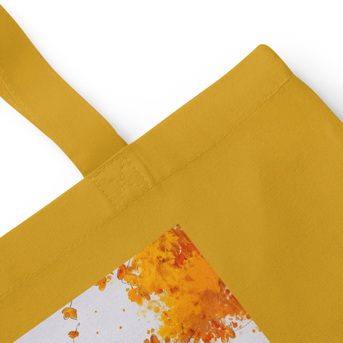 Close-up of a mustard yellow fabric tote bag corner with a printed abstract orange and yellow design on a white background.
