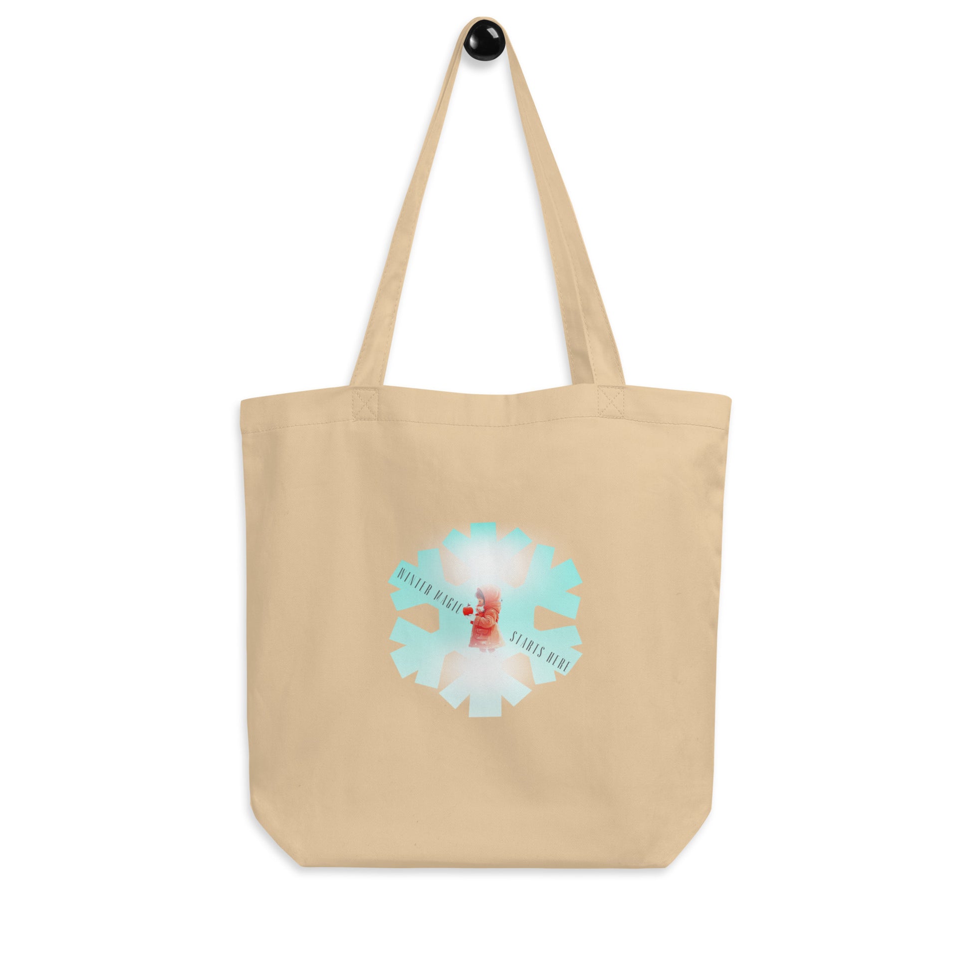 Front view of a natural-colored organic cotton tote bag with a 'Winter Magic Starts Here' snowflake graphic.