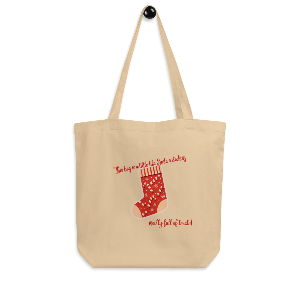 A beige canvas tote bag with a Christmas-themed graphic of a red stocking with white polka dots and text reading 'This bag is a little like Santa's stocking, mostly full of treats!' on a plain white background.