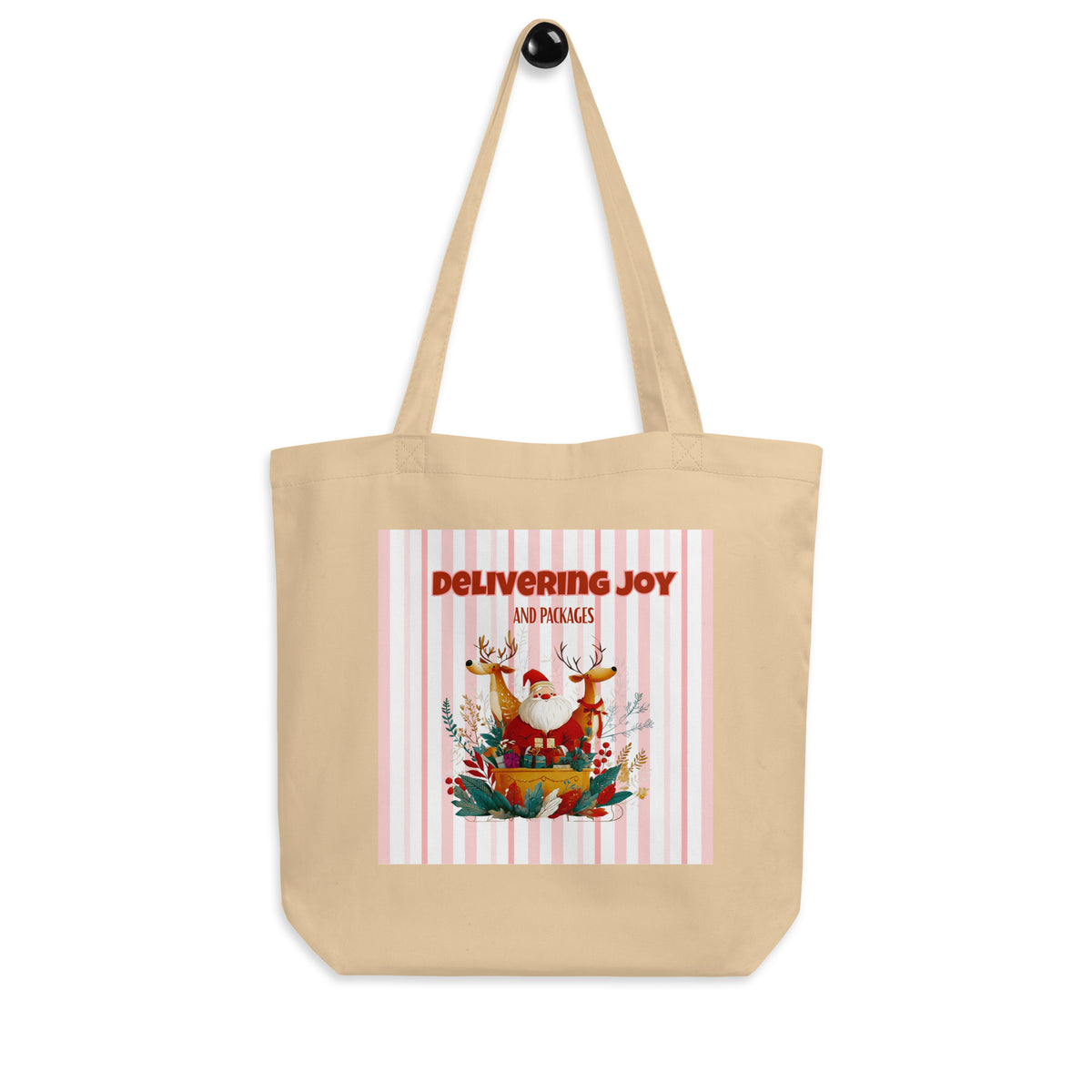 A beige canvas tote bag with two shoulder straps, featuring a festive Christmas graphic on the front with the text 'DELIVERING JOY AND PACKAGES' above an illustration of Santa in a sleigh with reindeer and holiday foliage.
