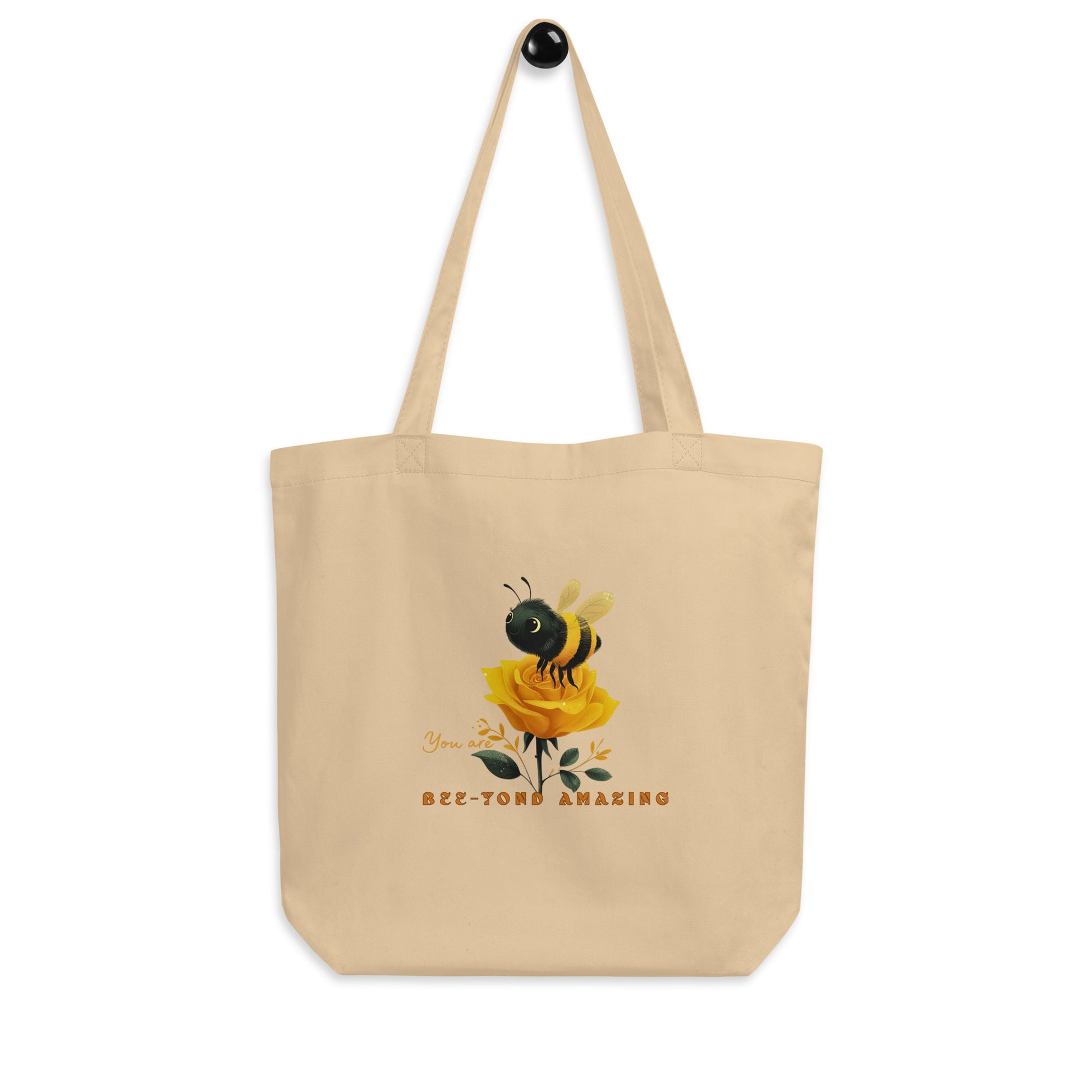 Beige eco tote bag with a bee and rose yellow rose design with the words 'You are Bee-yond amazing' on a white background. 
