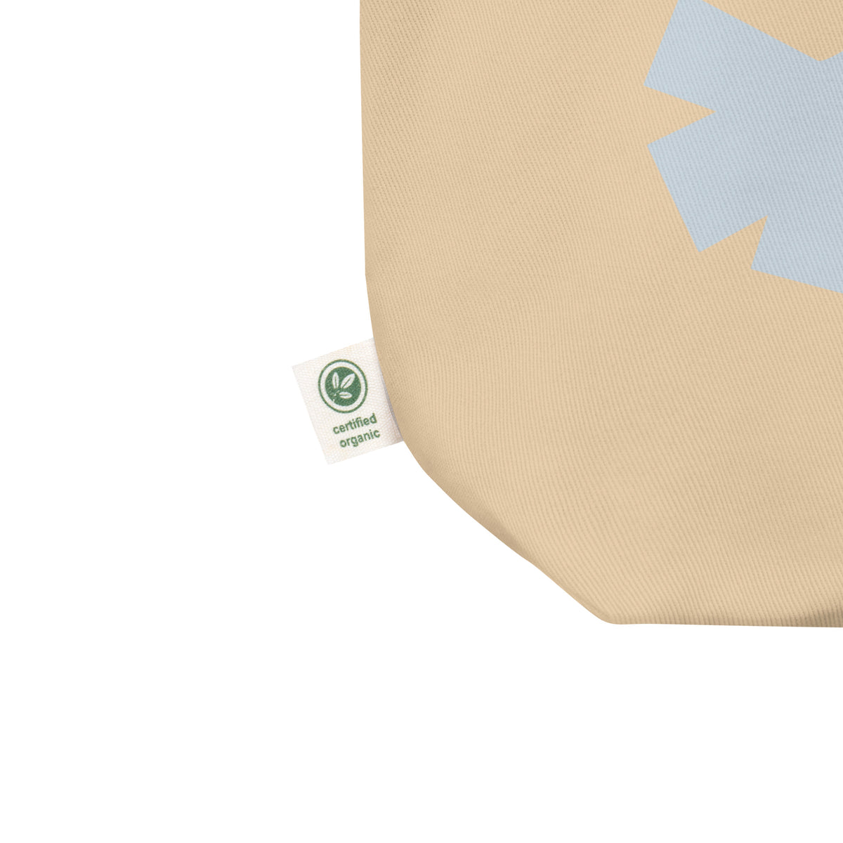 Close-up of a beige woven fabric product corner with a small white tag reading 'certified organic' and a light blue geometric accent on the fabric.