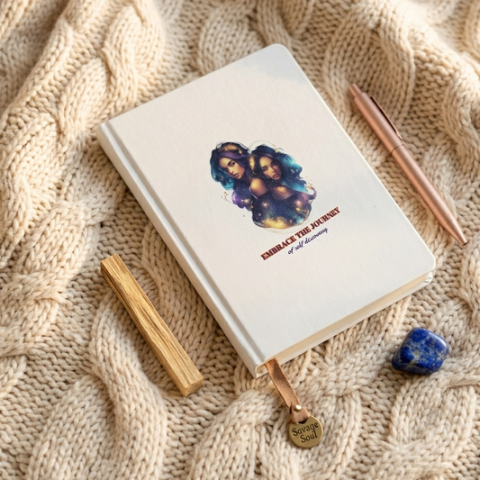 Lifestyle mockup of 'Embrace the Journey' Gemini zodiac notebook on a soft cable-knit blanket. Features the white hardcover journal with colorful twins graphic, a rose gold pen, a blue crystal, and a 'Savage Soul' leather bookmark in a cozy, mindful setting.