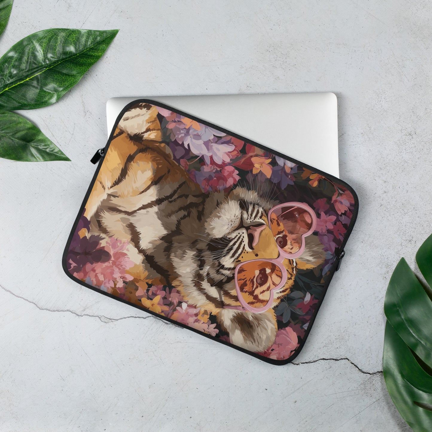 Artistic laptop sleeve featuring a bold tiger illustration wearing pink heart-shaped glasses, surrounded by purple and orange flowers, displayed as a product mockup on a light gray surface with green leaves.