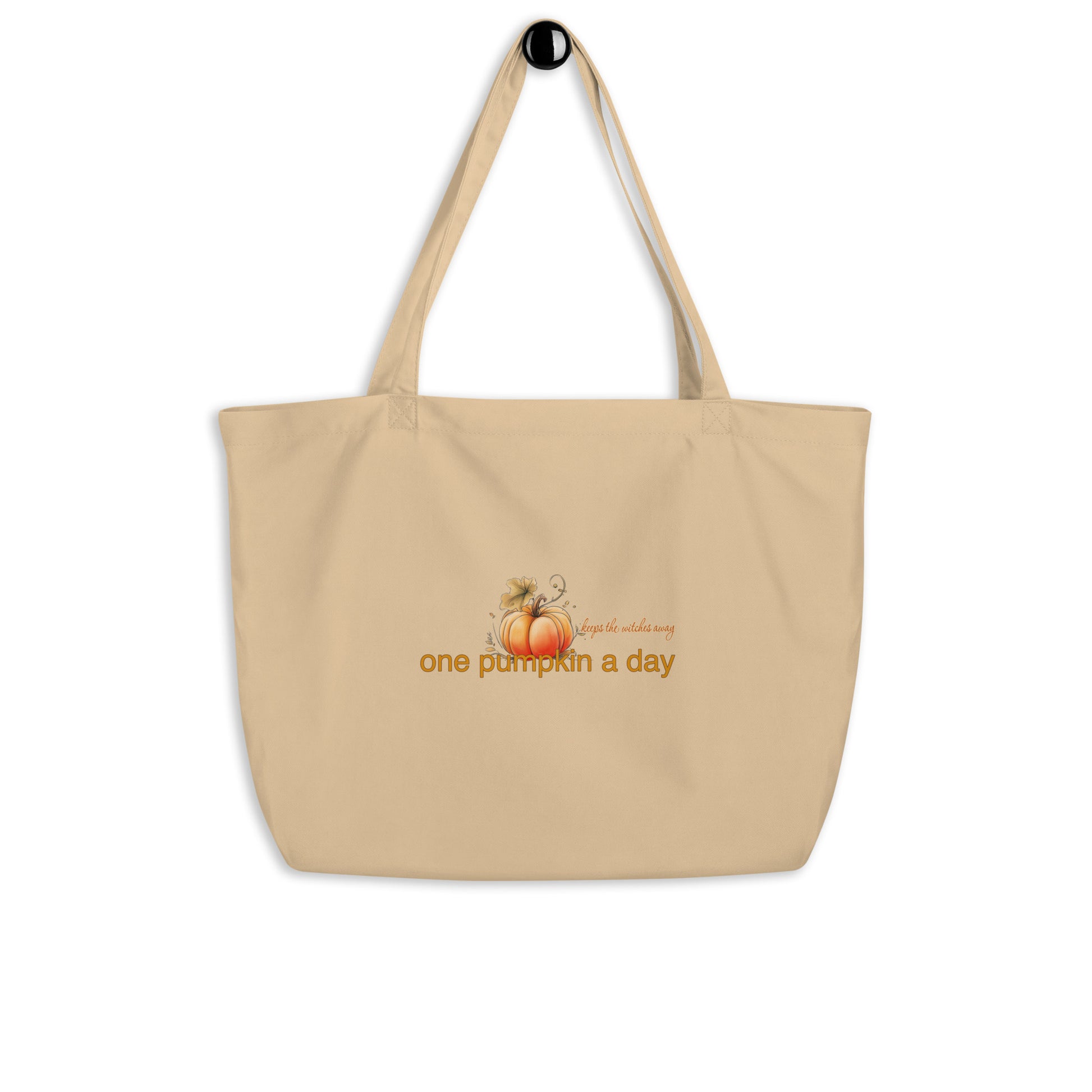 A beige canvas tote bag with two shoulder straps, featuring a graphic of a small orange pumpkin and the text 'One pumpkin a day, keeps the witches away' in orange on the front, shown against a plain white background.