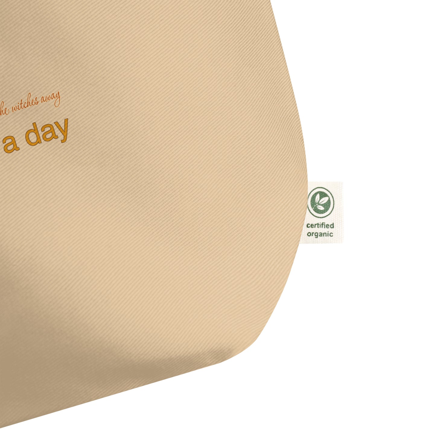 Close-up of a beige canvas tote bag corner showing partial orange text and a small green Certified Organic tag on a white background.