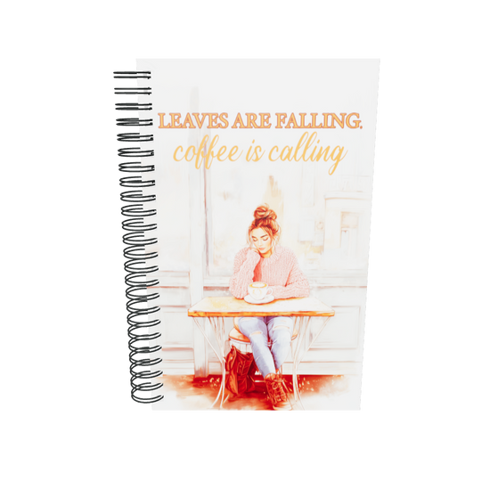 Spiral notebook with 'Leaves Are Falling, Coffee Is Calling' autumn illustration. Mockup shows a girl in a pink sweater at a café. Premium stationery for journaling and sketching.