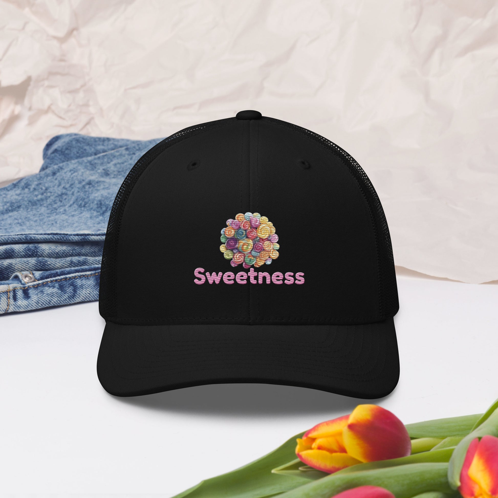 Black cap with 'Sweetness' text and a graphic of colourful candies on a floral background. 