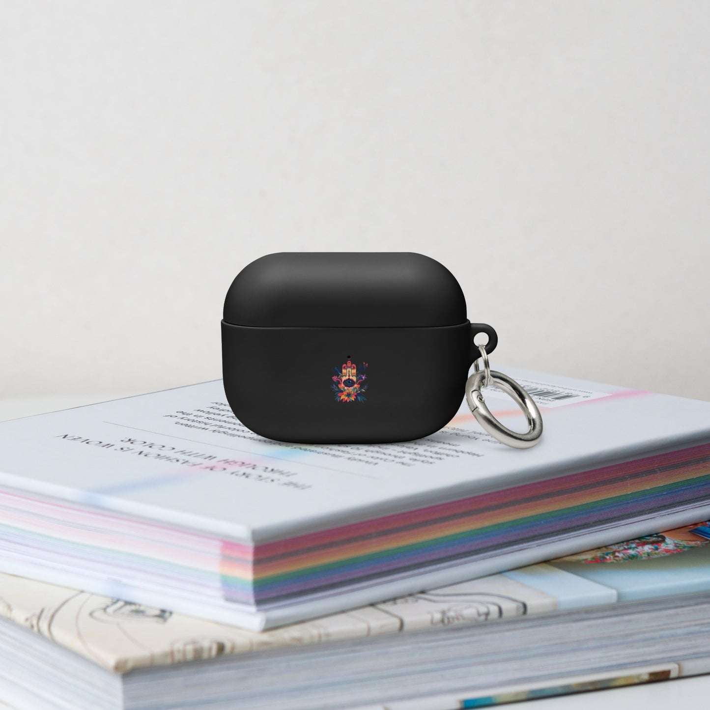 Black wireless earbud case with a keychain on top of colorful books