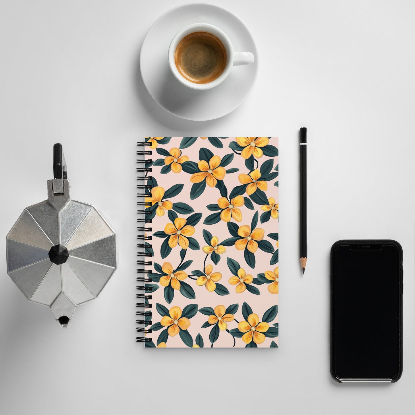 Spiral notebook with a delicate yellow and black floral pattern on a desk next to a coffee cup and a smartphone.