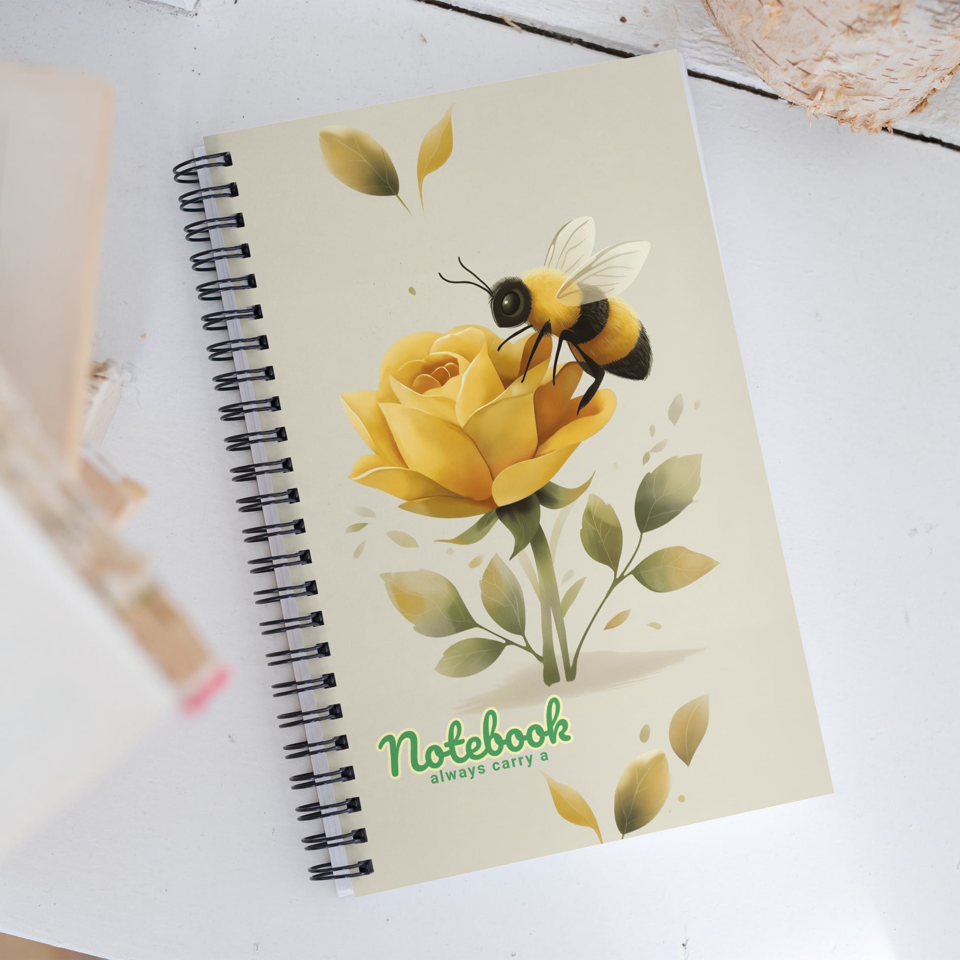 Spiral notebook with a design of a bee on a yellow rose with the text 'Always carry a notebook', on a white background.