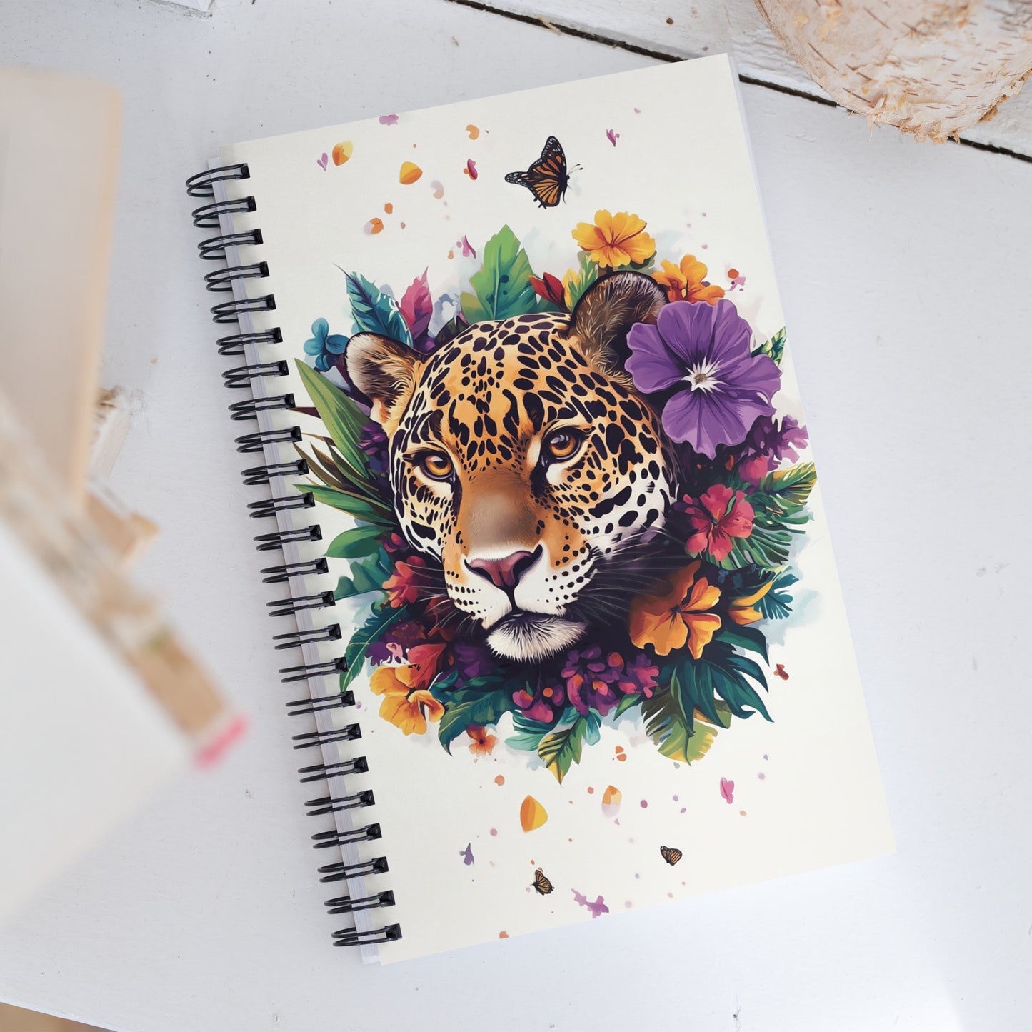 Spiral notebook with a colorful design of a jaguar surrounded by colorful flowers on a white surface.