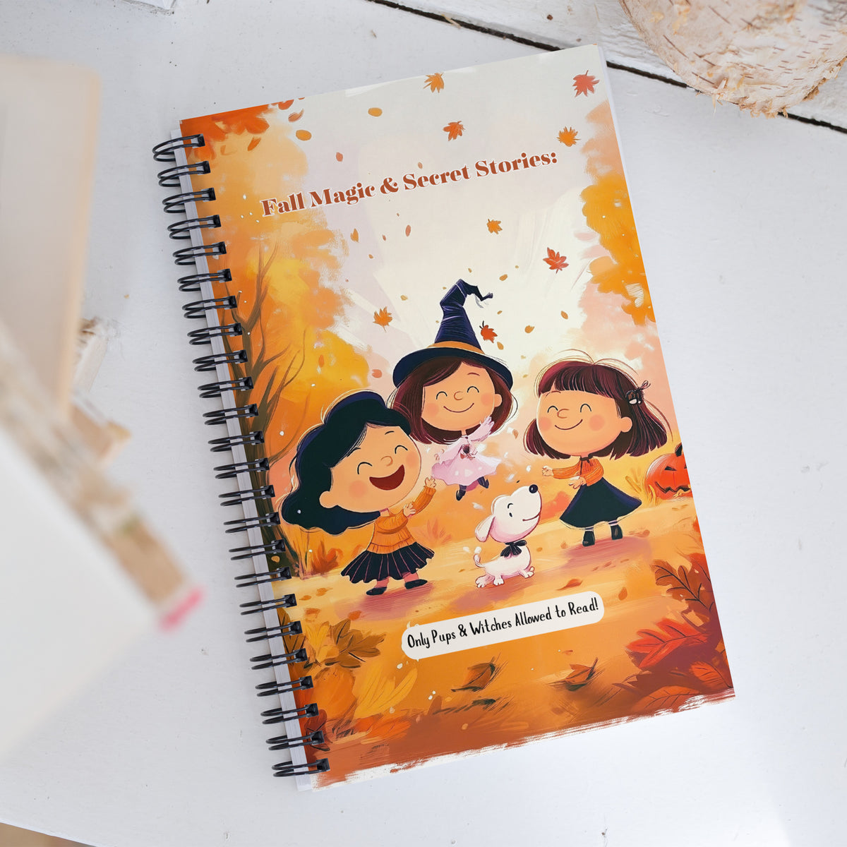 A spiral-bound notebook with a colorful autumn illustration on the cover, placed on a white surface with a neutral textured background.