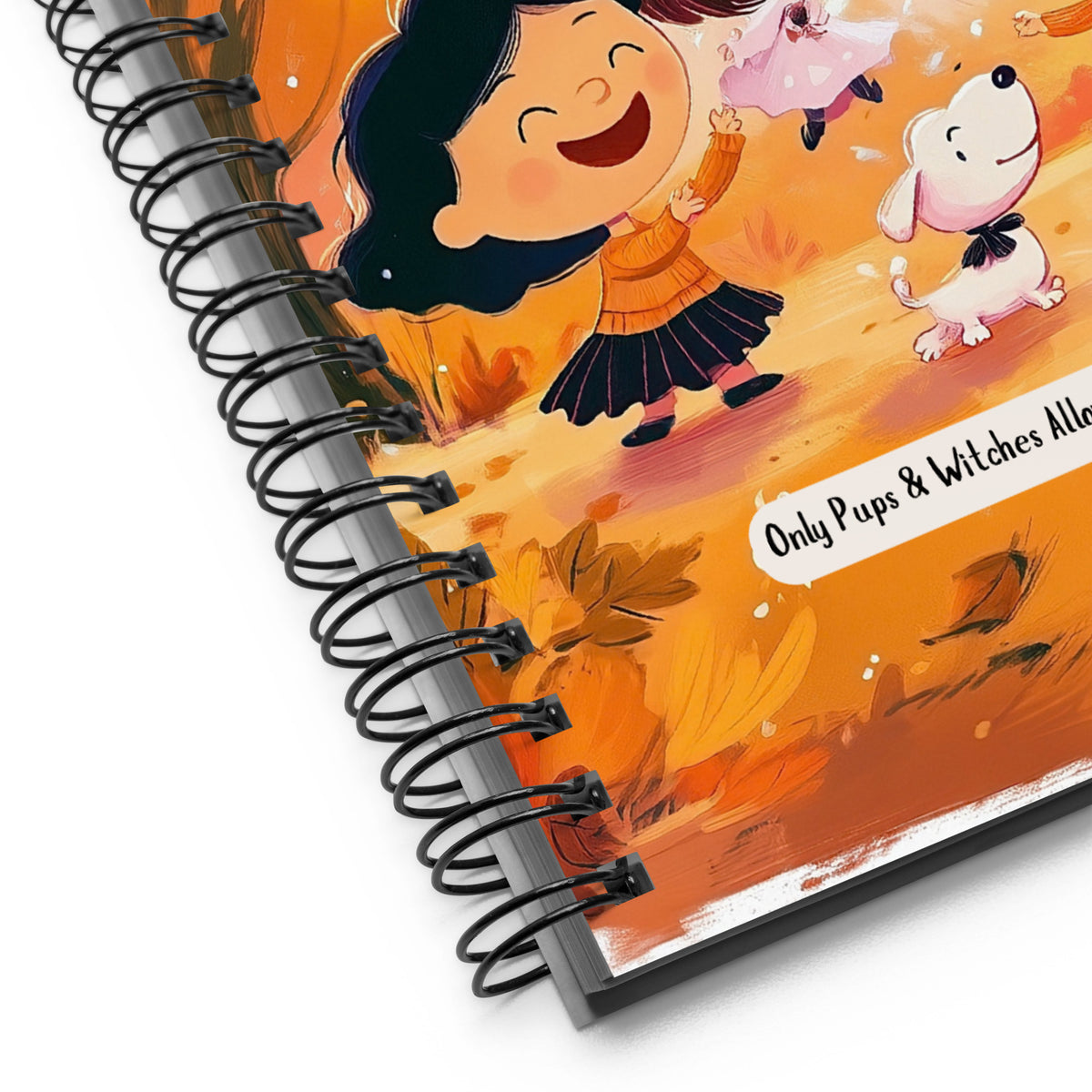 A close-up of a spiral-bound notebook showing a colorful autumn illustration with a smiling girl, a white dog, and leaves. The cover includes the text 'Only Pups & Witches Allow' on a white banner.