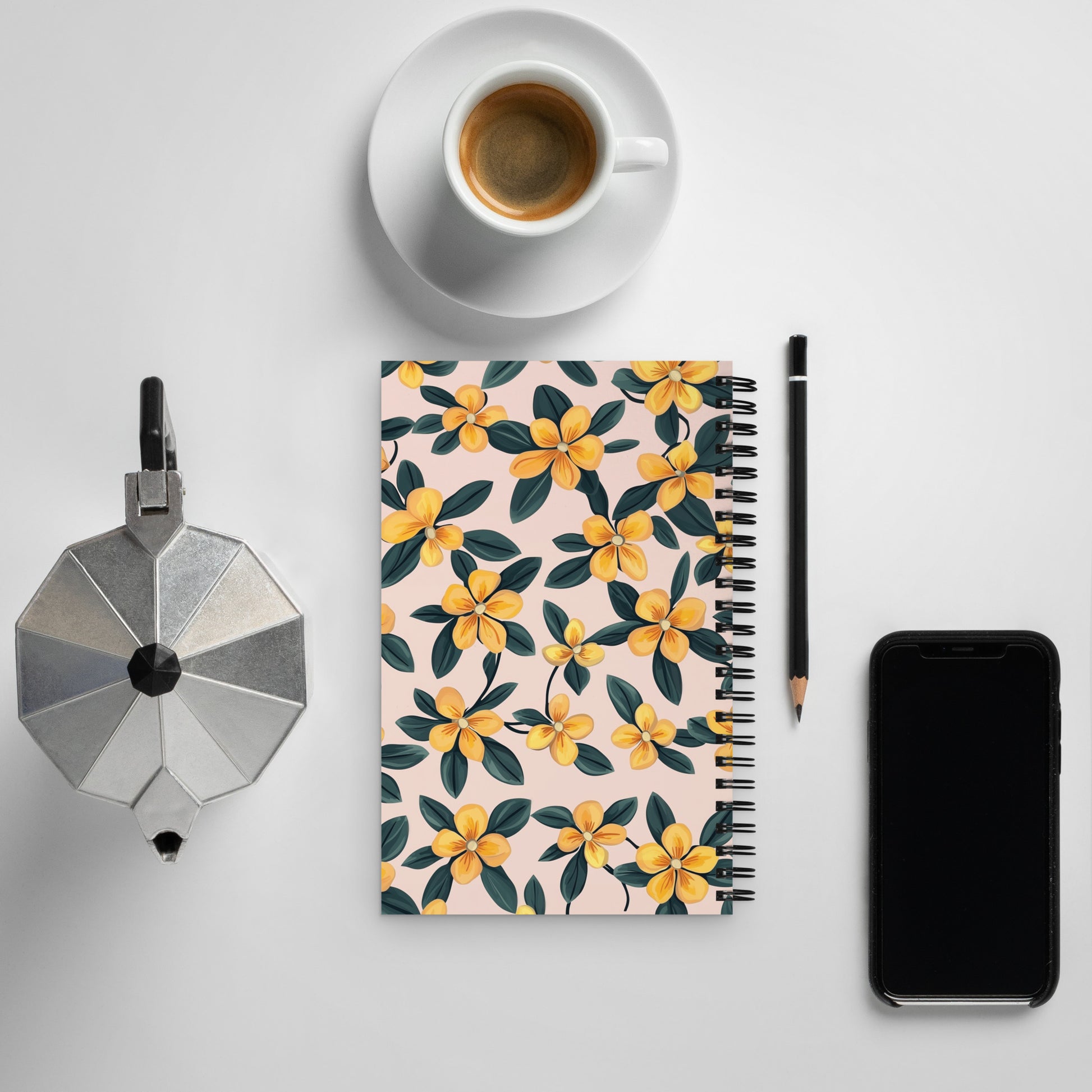Spiral notebook with a delicate yellow and black floral pattern on a desk next to a coffee cup and a smartphone.