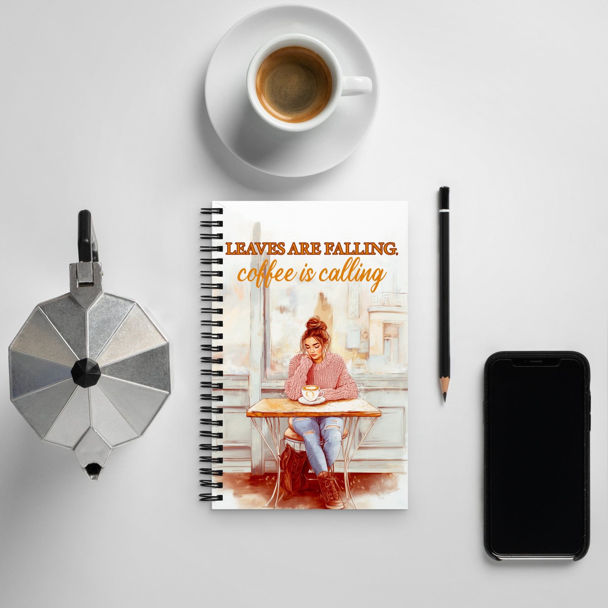 Spiral notebook with 'Leaves Are Falling, Coffee Is Calling' autumn illustration. Mockup shows a girl in a pink sweater at a café. Premium stationery for journaling and sketching.