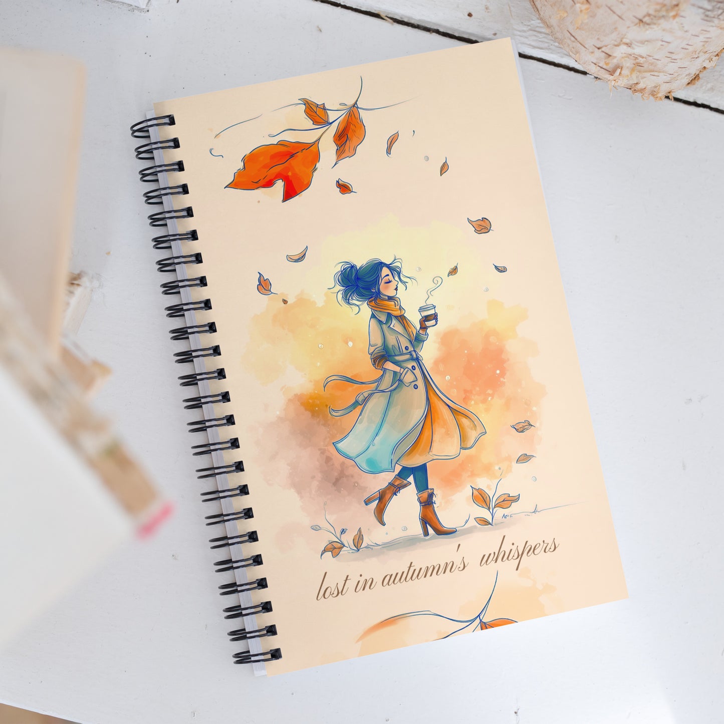 Notebook with a colorful illustration of a young woman in an autumn setting on a white surface.