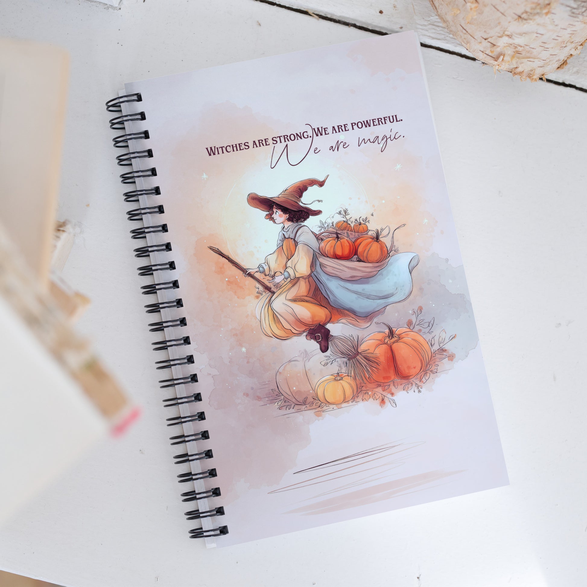 Spiral Notebook with a witch illustration and pumpkin design on a white surface by Sweet and Savage. 