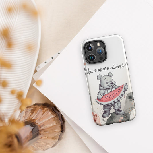 A clear phone case featuring a cute cartoon bear holding a watermelon slice with the text 'You're one in a watermelon!' printed on it, displayed on a white phone over a styled flat-lay background.